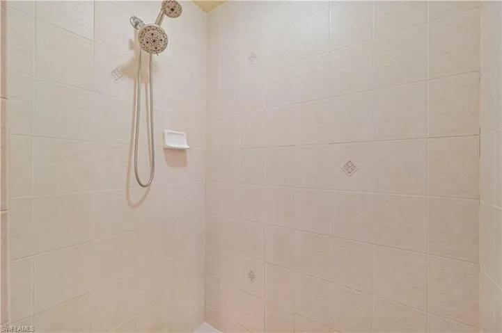 Shower enclosure featuring light-toned square wall tiles with decorative accent tiles