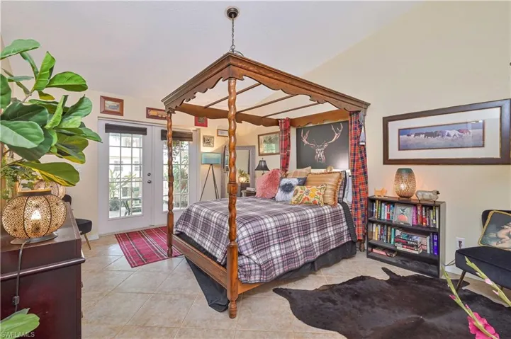 Spacious room featuring vaulted ceilings, neutral-toned tile flooring, and double French doors with transom windows