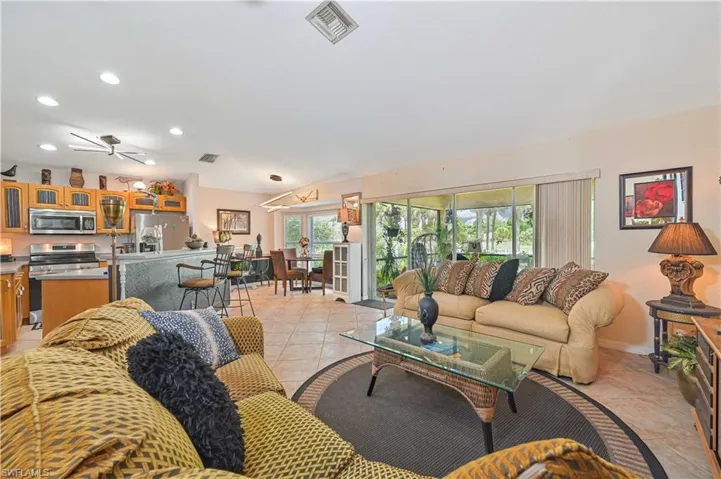 Open-concept living area with tile flooring throughout, featuring a kitchen with wood cabinetry and stainless steel appliances, a breakfast bar, and a dining area with outdoor access