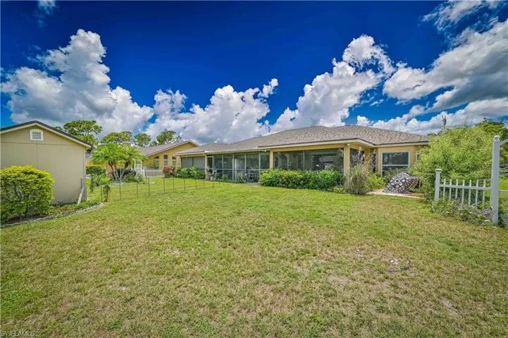 Expansive grassy yard area with a large screened-in porch, a separate storage shed, and a decorative white picket fence section