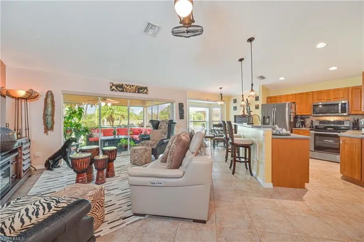 Spacious open-concept living area featuring neutral tile flooring, a screened lanai, and a kitchen with wood cabinetry and stainless steel appliances