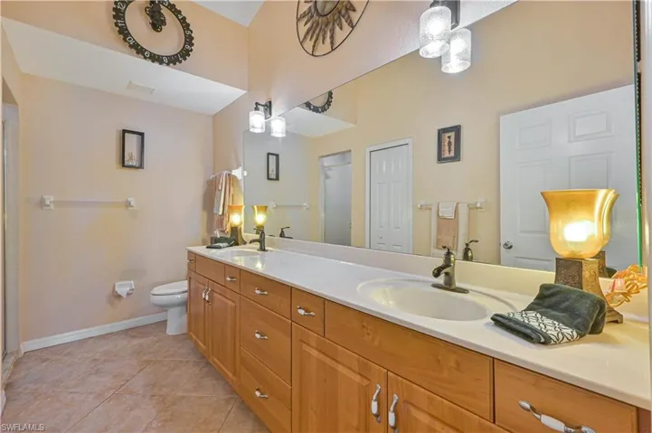 Double vanity with light wood cabinetry, white countertops, dual integrated sinks, and bronze-finish faucets