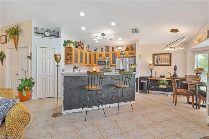 Open-concept kitchen and dining area featuring light-toned cabinetry, stainless steel appliances, and a breakfast bar with a textured dark-colored facade