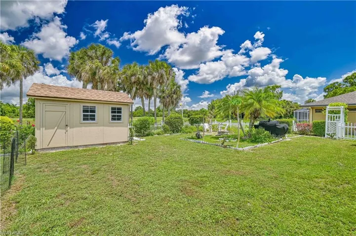 Expansive grassy yard featuring a detached storage shed with dual windows and a side entry door, mature palm trees, and perimeter fencing