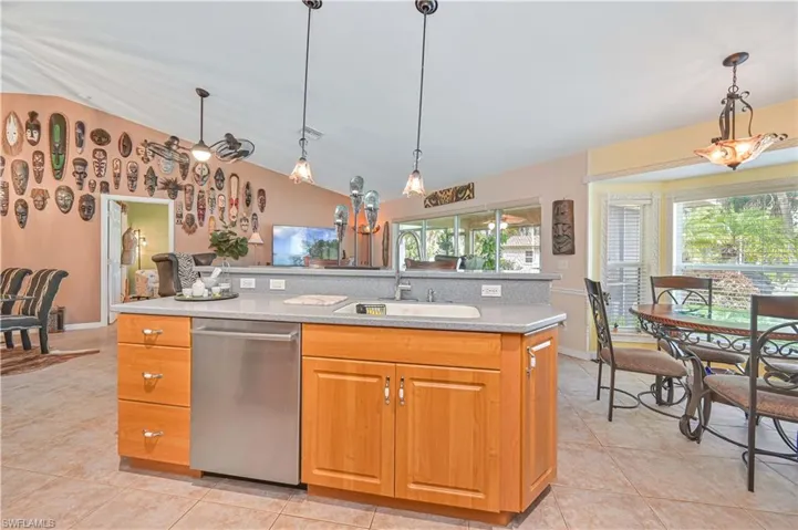 Kitchen island featuring wood cabinetry, integrated stainless steel dishwasher, and a stone-finish countertop with a double-basin sink