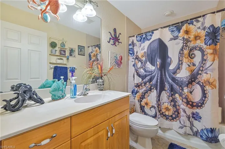 Wood-finish vanity with a single basin sink and a light-colored countertop, complemented by a large wall-mounted mirror and overhead vanity lighting