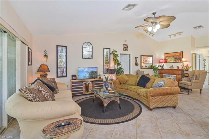Spacious living area featuring vaulted ceilings with a ceiling fan, tile flooring throughout, and sliding glass doors
