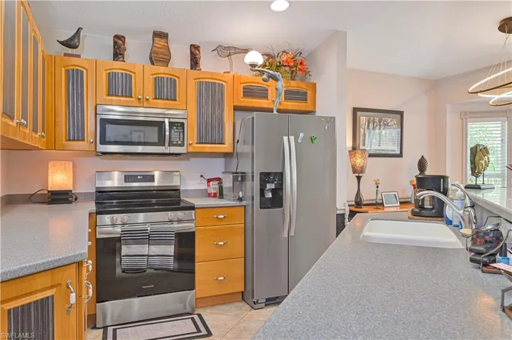 Kitchen featuring light wood cabinetry with reeded glass inserts, stainless steel appliances, and solid surface countertops