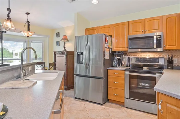 Kitchen featuring light wood cabinetry, stainless steel appliances, tile backsplash, and composite countertops