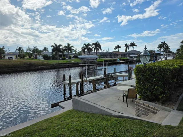 Waterfront property featuring a private boat dock with lifts, a concrete patio, a brick retaining wall, and mature landscaping