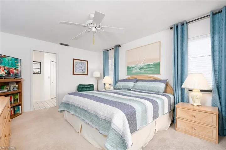 Carpeted bedroom featuring a ceiling fan, two windows with blinds, and an open doorway revealing tile flooring beyond