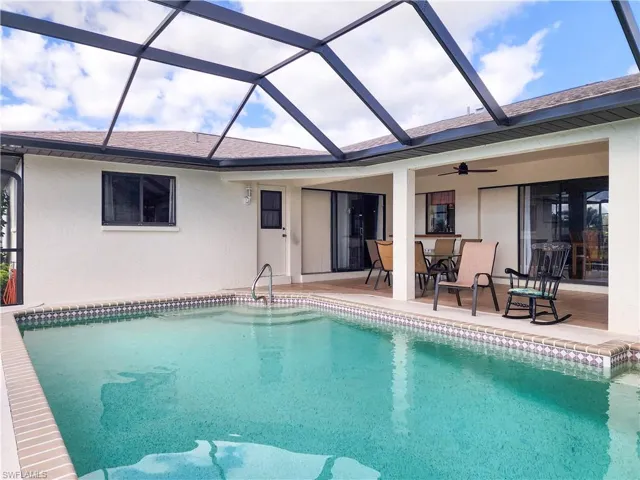 Screened-in pool deck featuring an in-ground swimming pool with steps, a covered patio with a ceiling fan, and sliding glass doors providing access to the interior