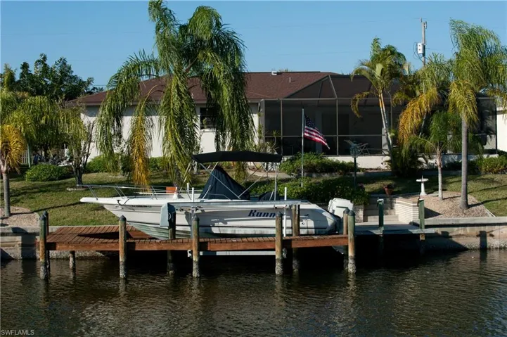 Waterfront property featuring a private wooden dock, screened-in patio, and mature palm trees