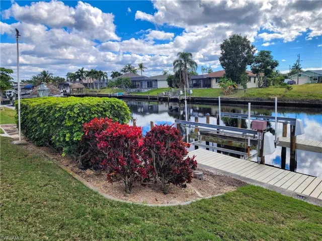 Waterfront property featuring a private boat dock with a lift, manicured lawn, and lush landscaping