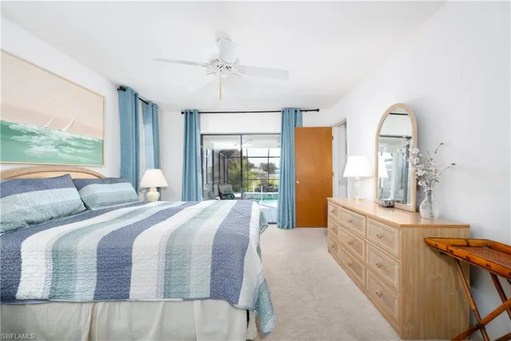 Carpeted bedroom with a ceiling fan, a light wood-tone dresser, and sliding glass doors opening to an exterior screened enclosure with a visible pool