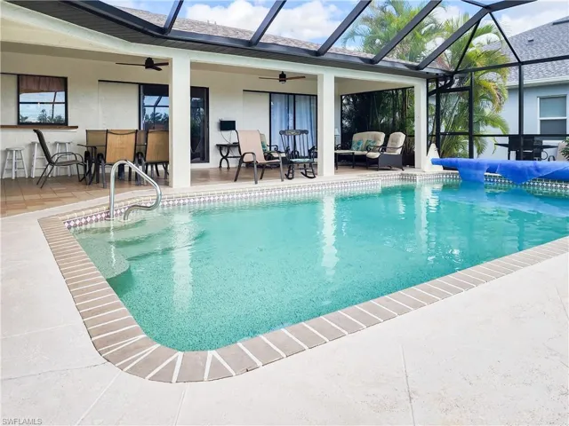 Screened-in swimming pool featuring a tiled waterline, integrated grab rail, and surrounding patio pavers
