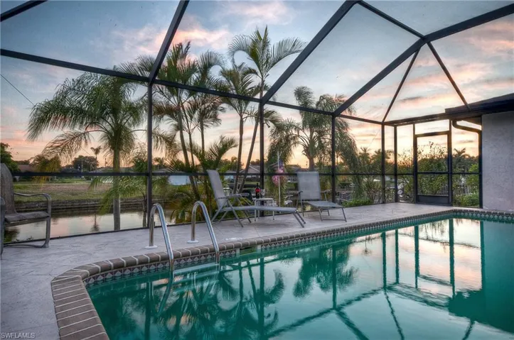 Screen-enclosed pool area featuring a rectangular pool with an attached ladder, a decorative tiled border, and a concrete deck