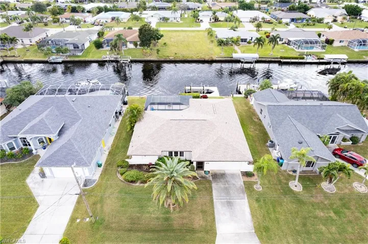 Waterfront property featuring a private boat dock, screened pool enclosure, paved driveway, and mature landscaping