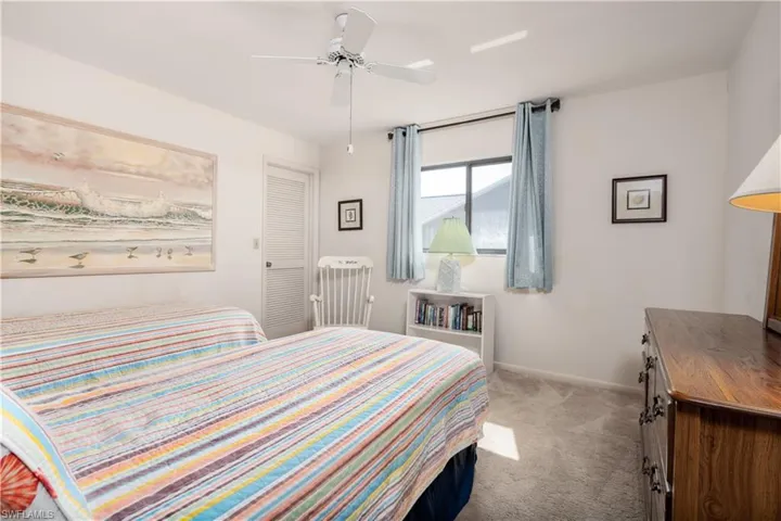 Room featuring a ceiling fan, window with light blue curtains, a louvered door, and carpet flooring