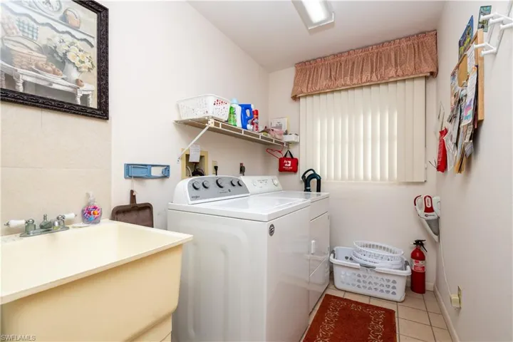 Dedicated laundry space featuring a utility sink with a dual-handle faucet, a window with vertical blinds, tiled flooring, and overhead shelving