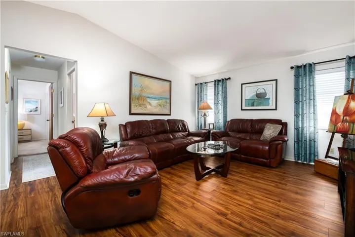 Living area featuring wood-finish flooring, vaulted ceiling, and white wall finishes