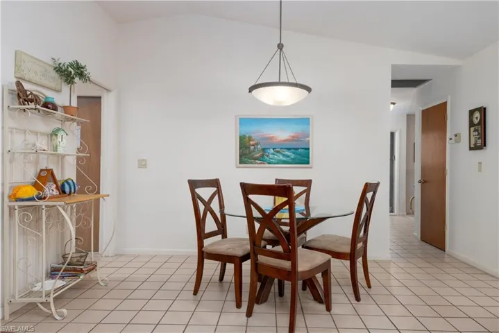 Dining area featuring a vaulted ceiling with a semi-flush mount light fixture, tile flooring, and white painted walls
