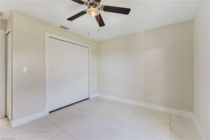 Unfurnished bedroom featuring light marble finish floors, a closet, and a ceiling fan