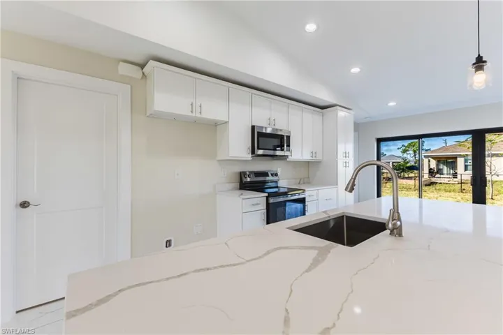 Kitchen featuring appliances with stainless steel finishes, recessed lighting, vaulted ceiling, pendant lighting, and white cabinetry