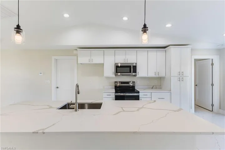 Kitchen featuring pendant lighting, appliances with stainless steel finishes, light stone counters, vaulted ceiling, and white cabinets