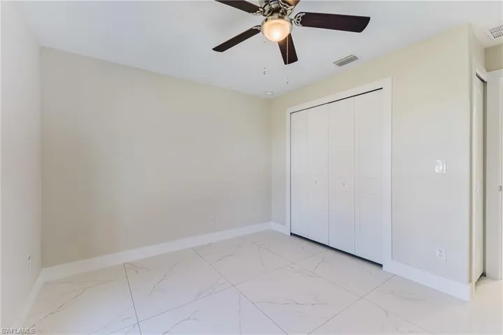Unfurnished bedroom featuring ceiling fan, light marble finish flooring, and a closet