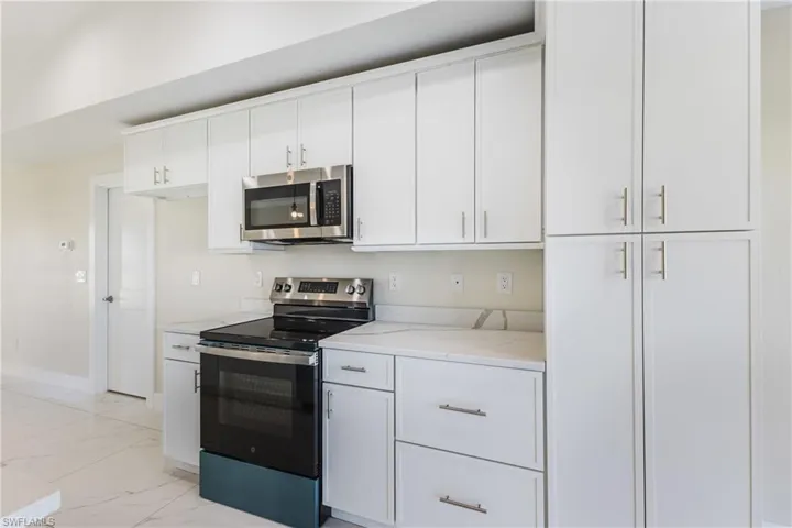 Kitchen featuring appliances with stainless steel finishes, white cabinets, light marble finish floors, and light stone counters