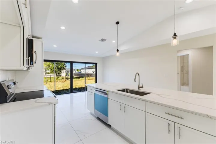 Kitchen with recessed lighting, white cabinets, light stone counters, hanging light fixtures, and lofted ceiling