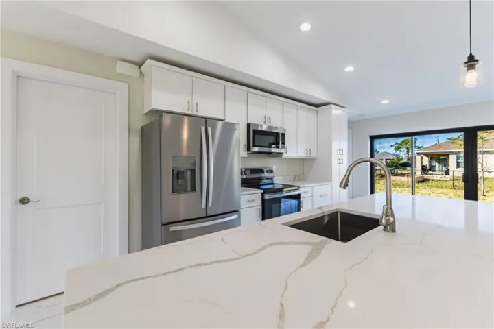 Kitchen featuring stainless steel appliances, recessed lighting, vaulted ceiling, light stone countertops, and white cabinets