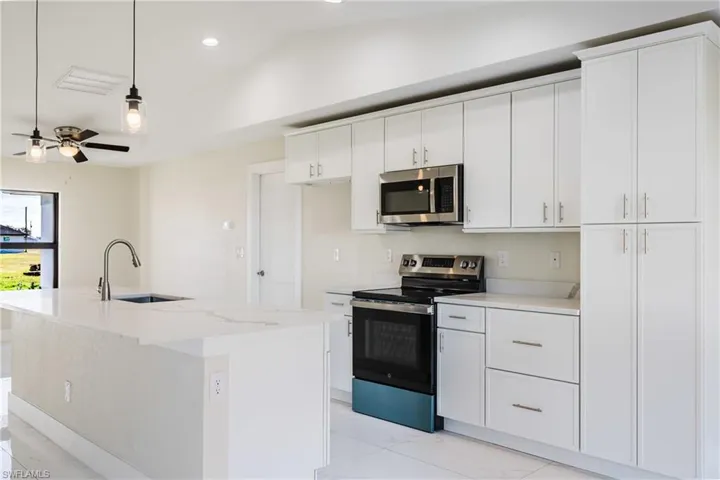 Kitchen featuring stainless steel appliances, light marble finish floors, decorative light fixtures, white cabinets, and recessed lighting