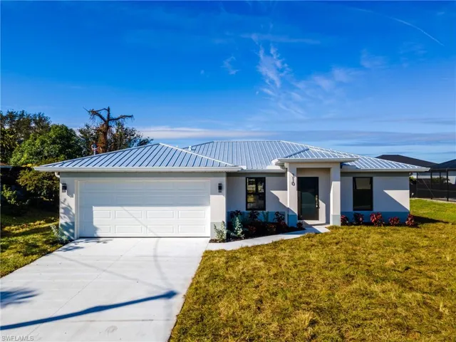 View of front facade with stucco siding, an attached garage, driveway, a front yard, and a metal roof