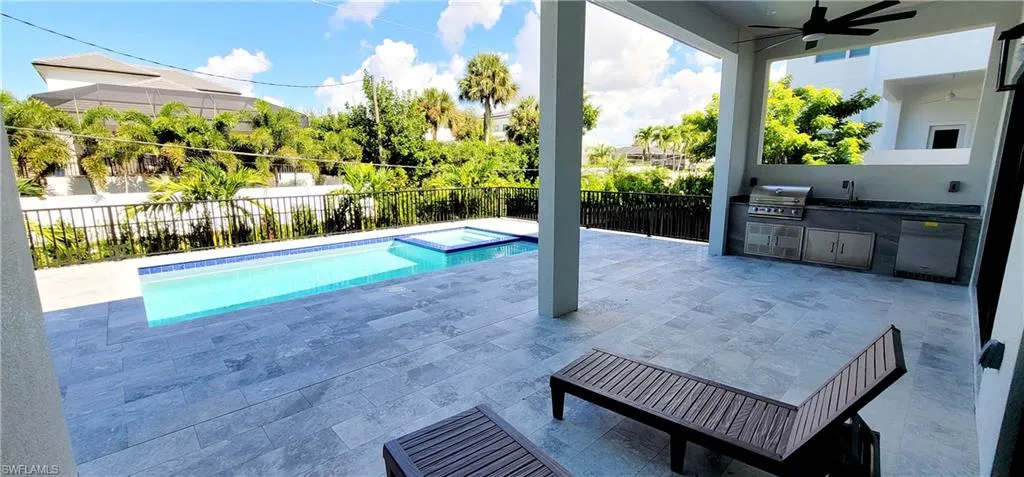 View of swimming pool with a ceiling fan, a pool with connected hot tub, a patio, exterior kitchen, and a fenced backyard