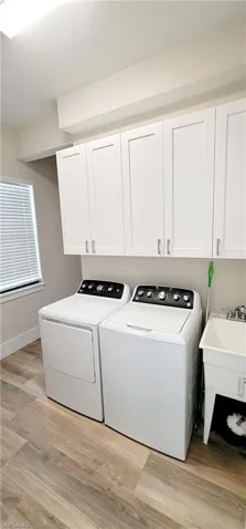 Laundry area with light wood-type flooring, cabinet space, and washing machine and clothes dryer