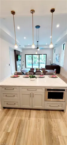 Kitchen featuring open floor plan, light stone counters, decorative light fixtures, light wood finished floors, and gray cabinetry