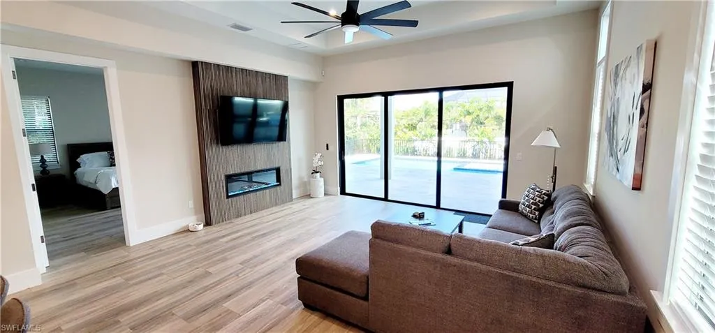 Living area with a large fireplace, light wood-type flooring, a tray ceiling, and ceiling fan