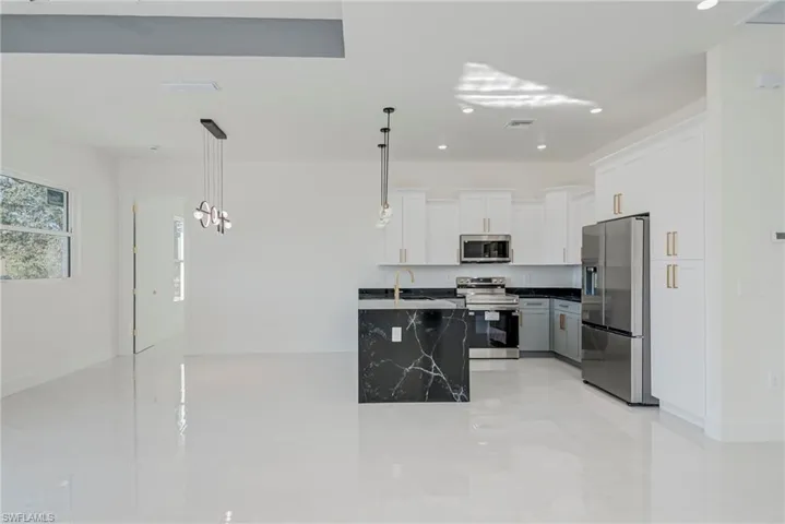 Kitchen featuring hanging light fixtures, stainless steel appliances, white cabinets, and dark stone countertops
