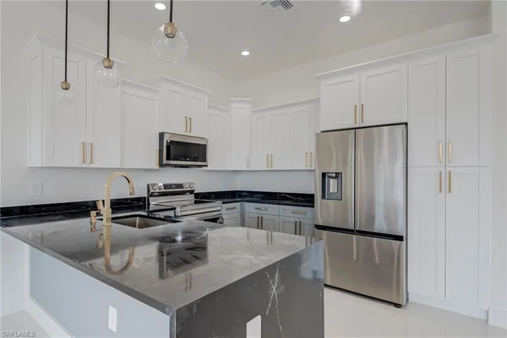 Kitchen with stainless steel appliances, dark stone counters, hanging light fixtures, white cabinetry, and a peninsula