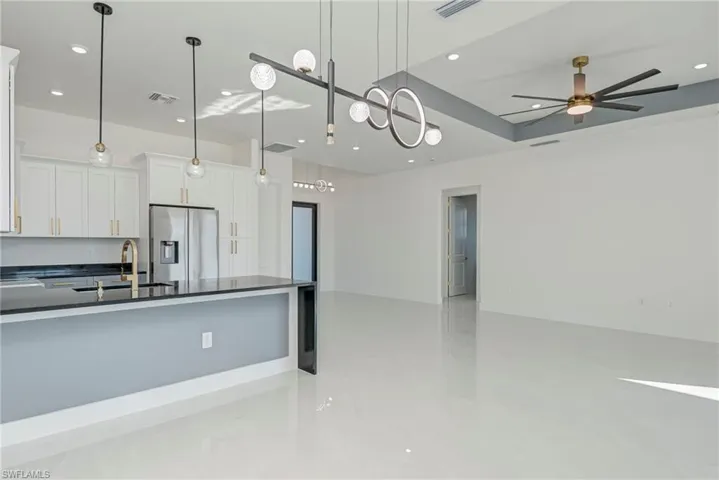 Kitchen featuring open floor plan, white cabinets, stainless steel fridge, decorative light fixtures, and a peninsula