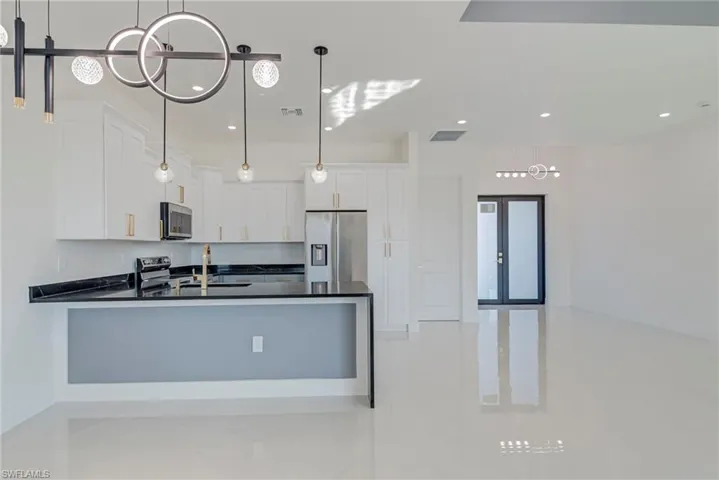 Kitchen featuring hanging light fixtures, stainless steel appliances, white cabinets, and a peninsula