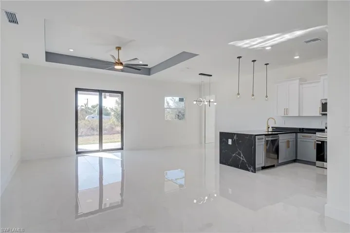 Dual tone kitchen with pendant lighting, open floor plan, a tray ceiling, two tone cabinets, and a ceiling fan
