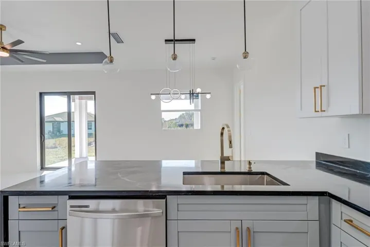 Kitchen featuring dark stone countertops, stainless steel dishwasher, pendant lighting, ceiling fan, and white cabinets