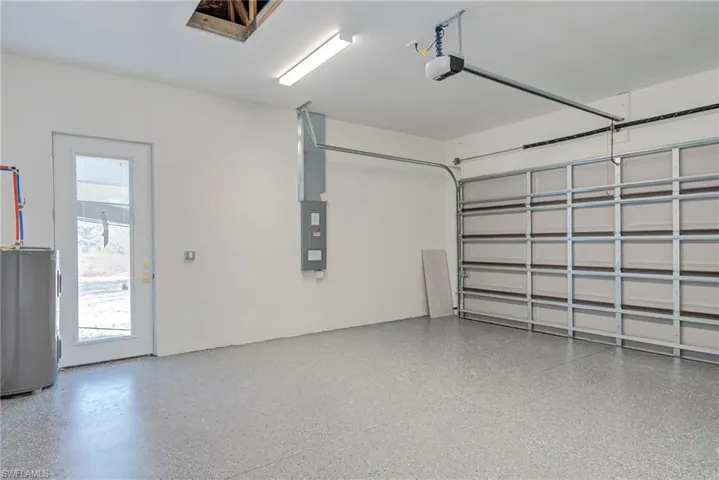 Garage with electric water heater, electric panel, and a garage door opener
