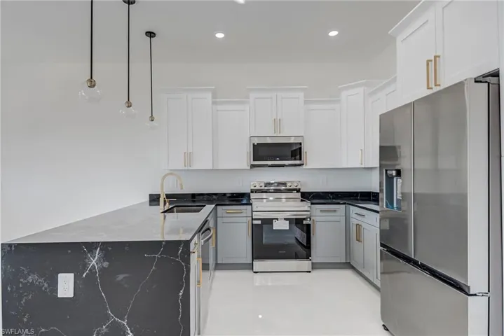 Two tone kitchen featuring stainless steel appliances, dark stone countertops, a peninsula, hanging light fixtures, and two tone cabinetry