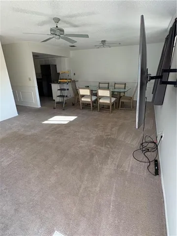 Carpeted dining area featuring a textured ceiling, a ceiling fan, and wainscoting