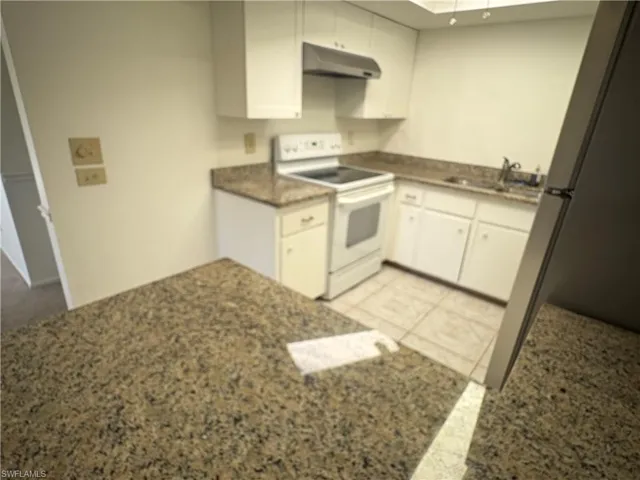 Kitchen with white cabinetry, white range with electric cooktop, light tile patterned flooring, and dark stone countertops