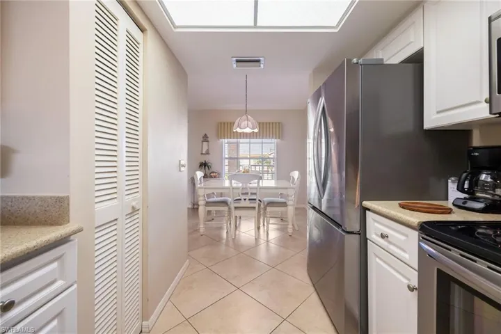Kitchen with white cabinets, light tile patterned floors, decorative light fixtures, stainless steel electric range, and light stone counters